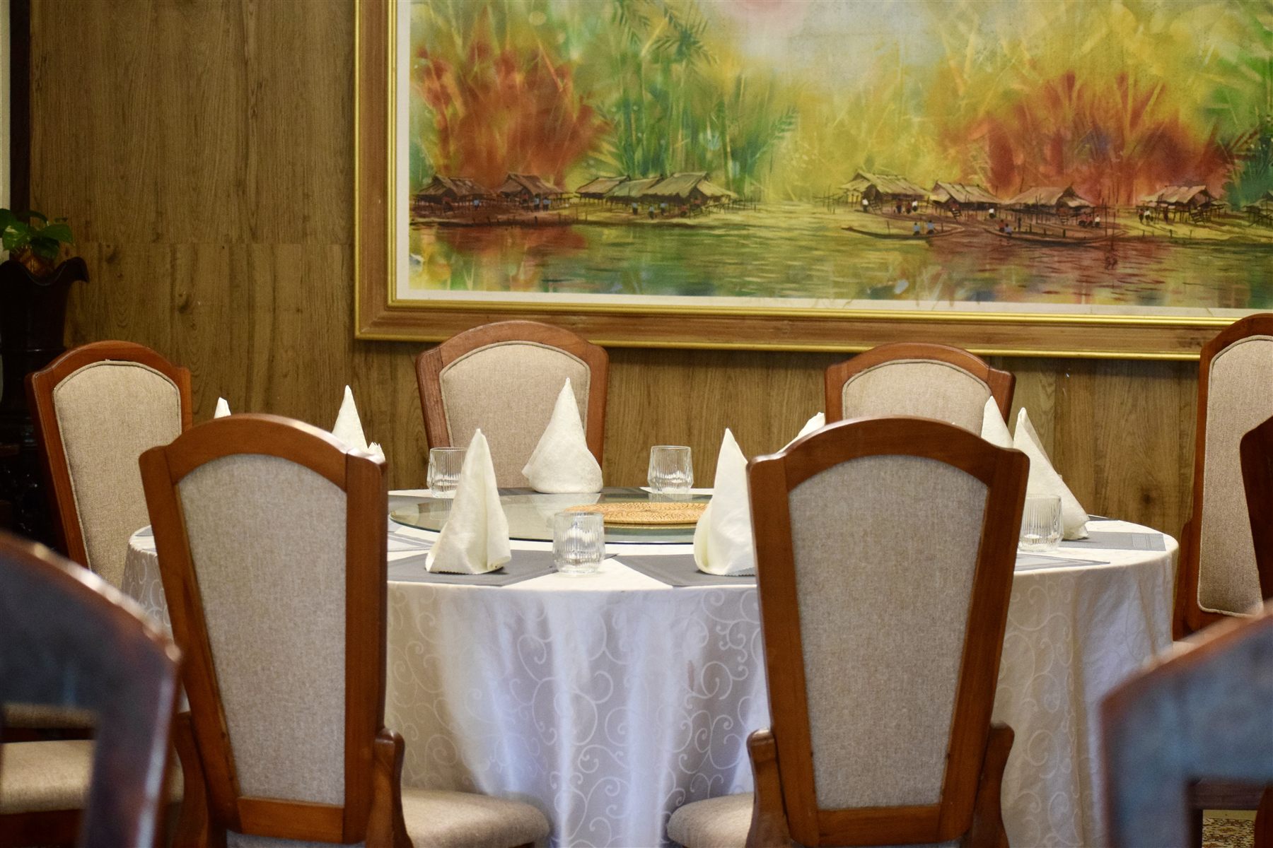 A round dining table beneath a Lao landscape painting